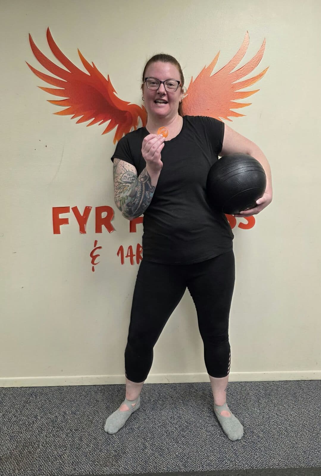 Member holding a medicine ball in front of the FYR Fitness logo